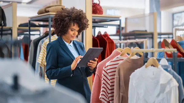 Clothing Store: Female Merchandising Manager Uses Tablet Computer To Create Stylish Fashion Collection. Professional Shop Sales Retail Assistant Checks Stock. Small Business Owner Orders Mall Items.