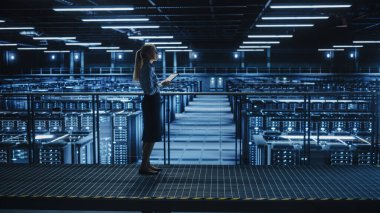 Veri Merkezi 'nde Tablet Bilgisayar kullanan kadın bilişim uzmanı, devasa sunucu çiftliği bulut hesaplama tesisine bakan bir köprüde yürüyor. Başarılı iş kadını, e-ticaret girişimcisi.
