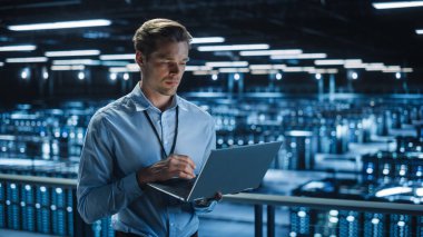 Data Center 'da dizüstü bilgisayar kullanan yakışıklı gülümseyen bilişim uzmanı. Başarılı İşadamı ve e-İş Girişimcisi Sunucu Çiftliği Bulut Hesaplama Tesisi.