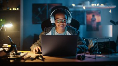 Dizüstü bilgisayar kullanan ve evdeki karanlık bir odada kulaklık takan çok ırklı genç bir kız. İnternette Eğitim Araştırmaları 'na bakıyor. Fen Fakültesi Ödevi Konsepti.