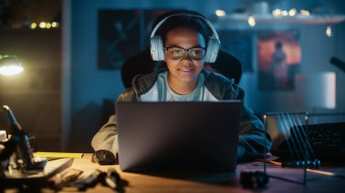 Dizüstü bilgisayar kullanan ve evdeki karanlık bir odada kulaklık takan çok ırklı genç bir kız. İnternette Eğitim Araştırmaları 'na bakıyor. Fen Fakültesi Ödevi Konsepti.