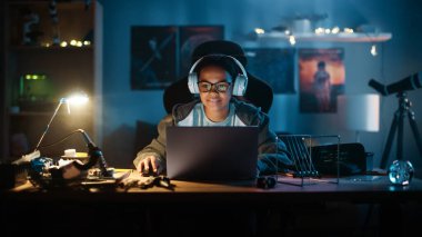 Dizüstü bilgisayar kullanan ve evdeki karanlık bir odada kulaklık takan çok ırklı genç bir kız. İnternette Eğitim Araştırmaları 'na bakıyor. Fen Fakültesi Ödevi Konsepti.