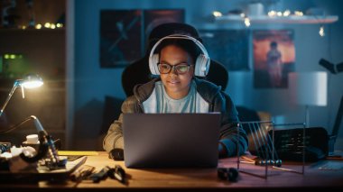 Dizüstü bilgisayar kullanan ve kulaklık takan çok ırklı genç bir kız evdeki karanlık bir odada. İnternette Eğitim Araştırmaları 'na bakıyor. Fen Fakültesi Ödevi Konsepti.