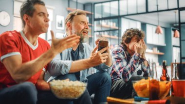 Ev: Üç Futbol Hayranı TV 'de Kanepede Oturuyor, Online Bet' e Akıllı Telefon Uygulaması Kullan, Futbol Takımı İçin Kaygılan. Arkadaşlar, tezahürat, haykırış, futbol maçı..