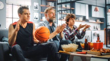 Ev Üç Mutlu Basketbol Hayranları TV 'de bir kanepede oturup maç seyrediyor, Sayı Turu ve Spor Takımı Şampiyonası' nı kutluyorlar. Arkadaşlar Grubu Favori Kulüp Oyunu Oynadığında Neşelenir.