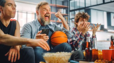 TV 'de Kanepede Oturan Üç Hayranlar Basketbol Maçı' nda, Skoru, İddiayı, İstatistikleri Kontrol Etmek için Akıllı Telefon Uygulamasını Kullan, Takım Şampiyonluğunu Kazandığında Kutla. Arkadaşlar Favori Kulüp Oyunu İzler