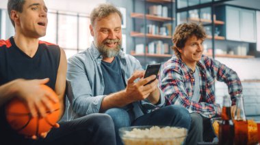 TV 'de Kanepede Oturan Üç Hayranlar Basketbol Maçı' nda, Skoru, İddiayı, İstatistikleri Kontrol Etmek için Akıllı Telefon Uygulamasını Kullan, Takım Şampiyonluğunu Kazandığında Kutla. Arkadaşlar Favori Kulüp Oyunu İzler