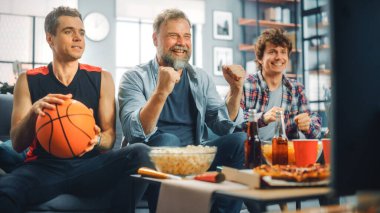 Home Three Happy Basketball fanları TV 'de bir kanepede oturup maç seyrediyor, Skorları kutluyor, Spor Takımı Şampiyonası' nı kazanıyorlar. Arkadaşlar Grubu, En İyi Kulüp Oyunu için Bağırın.