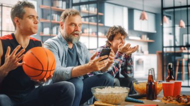 TV 'de Home Three Fans on Couch Watch Basketball Maçı' nda Score, Online Bet, Statistics, Team Wins Championship 'i kazananı kutlamak için Smartphone uygulamasını kullanın. Arkadaşlar Favori Kulüp Oyunu İzler