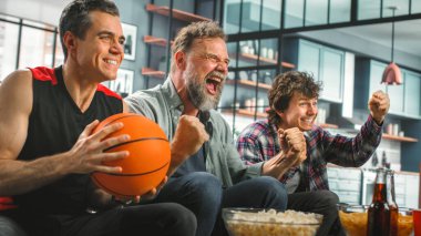 Home Three Happy Basketball fanları TV 'de bir kanepede oturup maç seyrediyor, Skorları kutluyor, Spor Takımı Şampiyonası' nı kazanıyorlar. Arkadaşlar Grubu, En İyi Kulüp Oyunu için Bağırın.