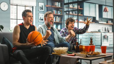 Ev Üç Mutlu Basketbol Hayranları TV 'de bir kanepede oturup maç seyrediyor, Sayı Turu ve Spor Takımı Şampiyonası' nı kutluyorlar. Arkadaşlar Grubu Favori Kulüp Oyunu Oynadığında Neşelenir.