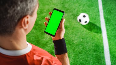 Profesyonel Futbolcu Akıllı Telefonu Yeşil Ekran Kroma Anahtarı ve İzleme İşaretleri ile Tutuyor. Futbol Yıldızının Sahada Ayakta Dururken İnterneti Kullanarak Omuz Üzerinden Üstten Aşağı Çekimi