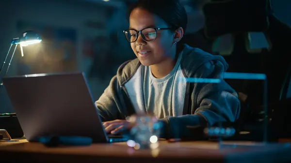 年轻的多种族黑人女孩在家中一间黑暗舒适的房间里使用笔记本电脑 她在网上浏览教育研究 理科学校作业概念 — 图库照片