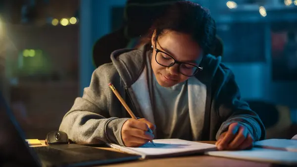 年轻的青少年多种族黑人女孩在笔记本上用铅笔写下作业 在家里黑暗舒适的房间里使用笔记本电脑 她在网上浏览教育学研究 — 图库照片