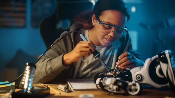 若い十代の多民族の女子高生は 彼女の科学ホビーロボットプロジェクトでエレクトロニクスとはんだ付けワイヤと回路基板を勉強しています 女の子は彼女の部屋でロボットに取り組んでいます 教育理念 — ストック写真