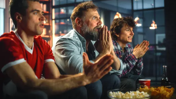 Night At Home: Three Joyful Soccer Fans Sitting on a Couch Watch Game on TV, Celebrate Victory when Sports Team Wins Championship. Group of Friends Cheer When Favourite Football Club Play.