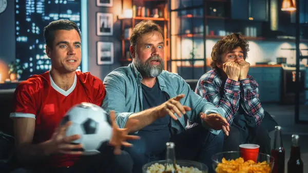 Night At Home: Three Joyful Soccer Fans Sitting on a Couch Watch Game on TV, Celebrate Victory when Sports Team Wins Championship. Group of Friends Cheer for Favourite Football Club Play.