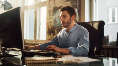 Genç Yakışıklı Adam, Otantik Çatı katında Yaratıcı Ajans 'ta bir Masaüstü Bilgisayarı' nda çalışıyor. Renovated Stylish Design with Artistic Posters and Big Windows.