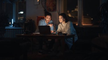 Yaratıcı Direktör ve Tasarımcı, Çatı katında Yaratıcı Ajans 'ta bir dizüstü bilgisayarda İşle İlgili Projeleri Tartışıyor. Bitkiler, Posterler ve Büyük Pencereli Karanlık Yenilenmiş Alan.