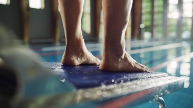 Bir başlangıç bloğunda duran ve yüzme havuzuna atlamaya hazırlanan kaslı Olgun Erkek Yüzücü. Sağlıklı Profesyonel Atletizm Şampiyonluğu Eğitimi. Güneş ışığıyla çekilen