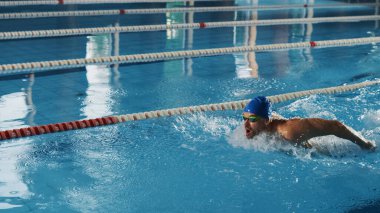 Bir başlangıç bloğunda duran ve yüzme havuzuna atlamaya hazırlanan kaslı Olgun Erkek Yüzücü. Sağlıklı Profesyonel Atletizm Şampiyonluğu Eğitimi. Güneş ışığıyla çekilen