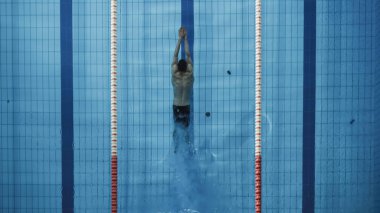 Bir başlangıç bloğunda duran ve yüzme havuzuna atlamaya hazırlanan kaslı Olgun Erkek Yüzücü. Sağlıklı Profesyonel Atletizm Şampiyonluğu Eğitimi. Güneş ışığıyla çekilen