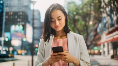 Çekici bir Japon kadın portresi. Üstü başı şık giyiniyor ve Şehir Caddesinde akıllı telefon kullanıyor. Büyük Şehir Yöneticisi Çevrimiçi İnsanlarla İletişim, Mesajlaşma ve İnternet Taraması.