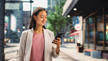 Çekici bir Japon kadın portresi. Üstü başı şık giyiniyor ve Şehir Caddesinde akıllı telefon kullanıyor. Büyük Şehir Yöneticisi Çevrimiçi İnsanlarla İletişim, Mesajlaşma ve İnternet Taraması.