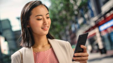 Çekici bir Japon kadın portresi. Üstü başı şık giyiniyor ve Şehir Caddesinde akıllı telefon kullanıyor. Büyük Şehir Yöneticisi Çevrimiçi İnsanlarla İletişim, Mesajlaşma ve İnternet Taraması.