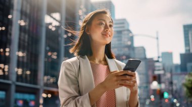 Çekici bir Japon kadın portresi. Üstü başı şık giyiniyor ve Şehir Caddesinde akıllı telefon kullanıyor. Büyük Şehir Yöneticisi Çevrimiçi İnsanlarla İletişim, Mesajlaşma ve İnternet Taraması.