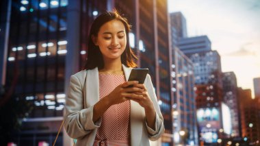 Çekici bir Japon kadın portresi. Üstü başı şık giyiniyor ve Şehir Caddesinde akıllı telefon kullanıyor. Büyük Şehir Yöneticisi Çevrimiçi İnsanlarla İletişim, Mesajlaşma ve İnternet Taraması.