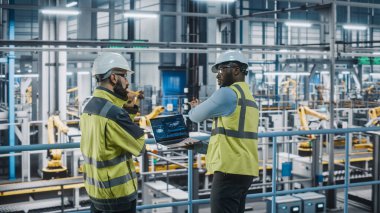 Dizüstü bilgisayar kullanan iki araba fabrikası yüksek görüş yeleği uzmanı. Otomotiv Endüstriyel Üretim Tesisleri Araç Üretimi Sürecini Tartışan Mühendisler. Otomatik Kurulum Tesisi.