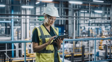 Yüksek Görüş Yelekli Kadın Araba Fabrikası Mühendisi Laptop kullanıyor. Otomotiv Endüstriyel Üretim Tesisi Robot Silahlarla Araç Üretimi üzerine çalışıyor. Otomatik Kurulum Tesisi.