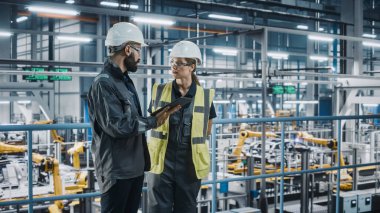 Erkek Uzman ve Kadın Araba Fabrikası Yüksek Görüş Yelekleri Mühendisi Tablet Bilgisayar kullanıyor. Otomotiv Endüstriyel Üretim Tesisi Araç Üretimi üzerine çalışıyor. Assembly Plant 'ta Çeşitlilik.