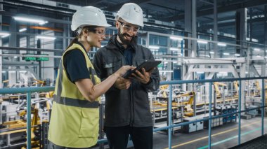 Erkek Uzman ve Kadın Araba Fabrikası Yüksek Görüş Yelekleri Mühendisi Tablet Bilgisayar kullanıyor. Otomotiv Endüstriyel Üretim Tesisi Araç Üretimi üzerine çalışıyor. Assembly Plant 'ta Çeşitlilik.