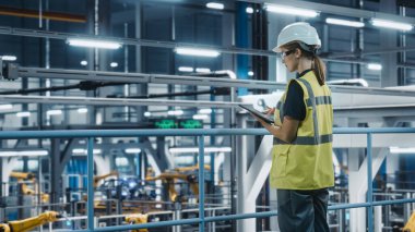 Yüksek Görüş Yelekli Kadın Araba Fabrikası Mühendisi Tablet Bilgisayar kullanıyor. Otomotiv Endüstriyel Üretim Tesisi Robot Teknolojisi ile Araç Üretimi üzerine çalışıyor. Otomatik Kurulum Tesisi.