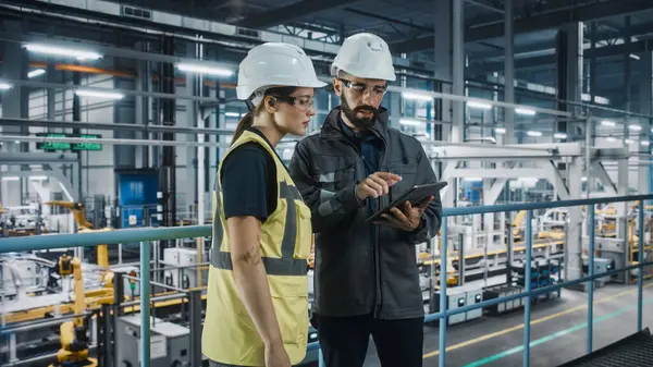 stock image Male Specialist and Female Car Factory Engineer in High Visibility Vests Using Tablet Computer. Automotive Industrial Manufacturing Facility Working on Vehicle Production. Diversity on Assembly Plant.