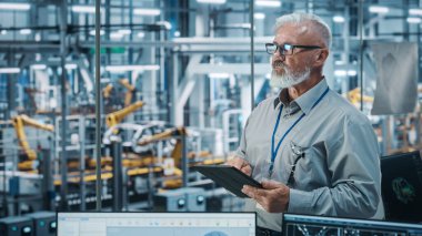 Otomatik Robot Silahlanma Hattı Üretim Hattı Yüksek Teknolojik Elektrikli Araçlar 'da Tablet Bilgisayar kullanan kıdemli Beyaz Erkek Mühendis Portresi. Orta Çekim