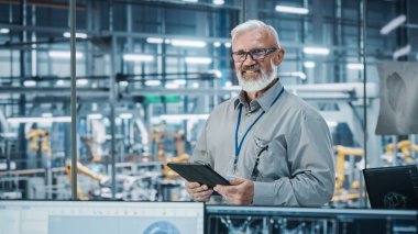 Otomatik Robot Silahlanma Hattı Üretim Hattı Yüksek Teknolojik Elektrikli Araçlar 'da Tablet Bilgisayar kullanan kıdemli Beyaz Erkek Mühendis Portresi. Kameraya bakarak ve gülümseyerek.