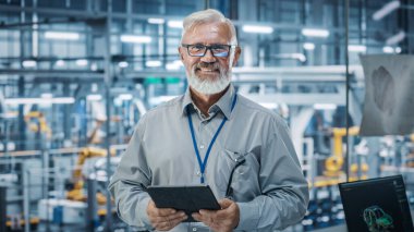 Otomatik Robot Silahlanma Hattı Üretim Hattı Yüksek Teknolojik Elektrikli Araçlar 'da Tablet Bilgisayar kullanan kıdemli Beyaz Erkek Mühendis Portresi. Kameraya bakarak ve gülümseyerek.