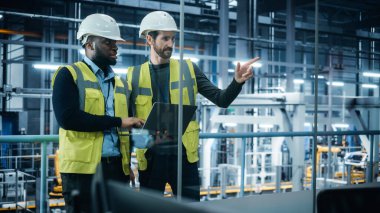 Araba Fabrikası: Proje Müdürü ve Hard Hat 'te Otomotiv Mühendisi, Konuşan, Laptop Kullanan. İzleme, Kontrol, Ekipman Üretimi. Otomatik Robot Silahlanma Hattı Üretim Elektrikli Araçlar