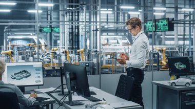 Gözlüklü ve Beyaz Gömlekli Yakışıklı Mühendis Tablet Bilgisayar kullanıyor ve bir araba montaj tesisinde ofisten dışarı bakıyor. Teknolojik Tesiste Araç Tasarımı üzerine çalışan Endüstriyel Uzman.