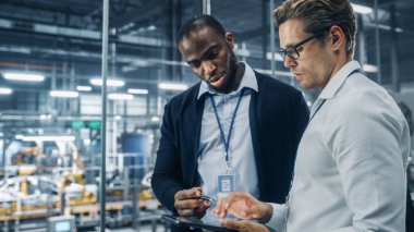 İki farklı otomotiv endüstrisi mühendisi bir otomobil montaj tesisinde çalışırken araç üretimi hakkında konuşuyor. Endüstriyel Uzmanlar Tablet Bilgisayarında Çalışma Projelerini Tartışıyor.