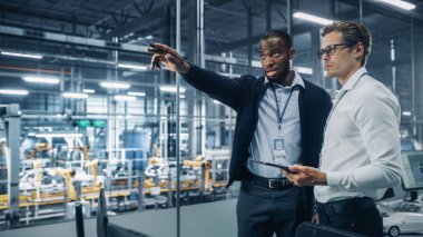 İki farklı otomotiv endüstrisi mühendisi bir otomobil montaj tesisinde çalışırken araç üretimi hakkında konuşuyor. Endüstriyel Uzmanlar Tablet Bilgisayarında Çalışma Projelerini Tartışıyor.