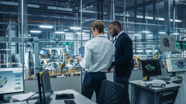 İki farklı otomotiv endüstrisi mühendisi bir otomobil montaj tesisinde çalışırken araç üretimi hakkında konuşuyor. Endüstriyel Uzmanlar Tablet Bilgisayarında Çalışma Projelerini Tartışıyor.