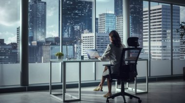 Successful Caucasian Businesswoman Sitting at Her Desk Working on Laptop Computer in Big City Office. Confident Corporation CEO Plan Investment Strategy for Disruptive e-Commerce Startup. Back View clipart
