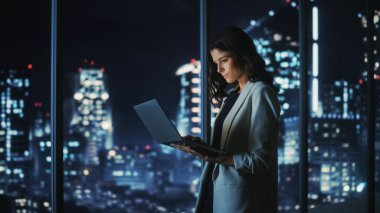 Geceleyin Büyük Şehir Modern Ofisi: Başarılı Genç İşkadını Ayakta Duruyor ve Dizüstü bilgisayar Kullanıyor. E-Ticaret için Yatırım Stratejisi Düşünen Güzel Dijital Girişimci.