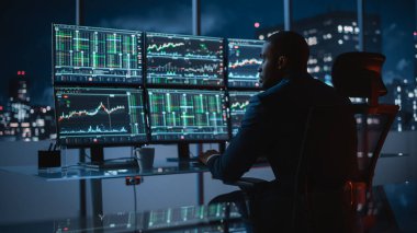 Gerçek zamanlı hisse senetleri, emtialar ve borsa grafikleriyle birlikte Multi-Monitor Workstation ile birlikte bir bilgisayar üzerinde çalışan serbest fon tüccarı. İşadamı Yatırım Bankası Şehir Merkezi Ofisinde Gece Çalışıyor.
