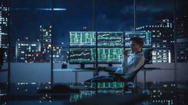 Finansal Analizci, Multi-Monitor Workstation ve Real-time Borsa ve Borsa Çizelgeleri ile bir bilgisayar üzerinde çalışıyor. İşadamı Yatırım Bankası Şehir Merkezi Ofisinde Gece Çalışıyor.