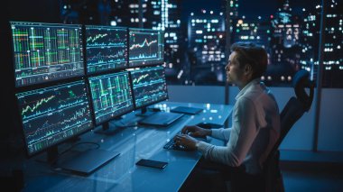 Finansal Analizci Multi-Monitor Workstation ve Real-time Stocks, Commodities ve Foreign Exchange Charts ile bir bilgisayar üzerinde çalışıyor. Yatırım Bankası Şehir Ofisinde İşadamı Gece Geç Saatlere Kadar Çalışıyor.